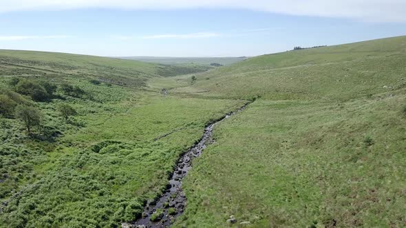 Very slow forward tracking aerial shot over a Dartmoor creek river with a perpendicular bend. Devon,