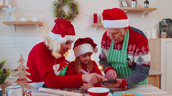 Senior Grandparents and Grandchild Watching Cooking Lesson Using Digital Tablet at Christmas Kitchen