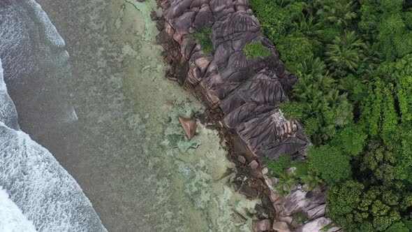 Aerial view of waves crashing along coastline of cliffs and palm trees La Digue Seychelles