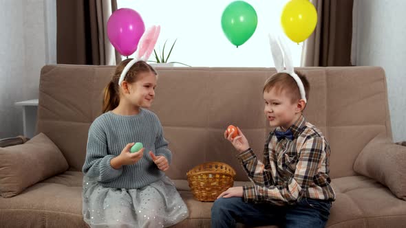 A Boy in White Bunny Ears and a Girl in Pink Bunny Ears Hold Easter Colored Eggs