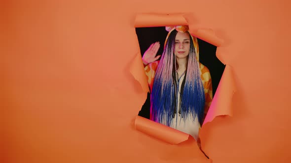 Young Woman in Pajamas of Giraffe Looking Out Through Hole of Orange Background