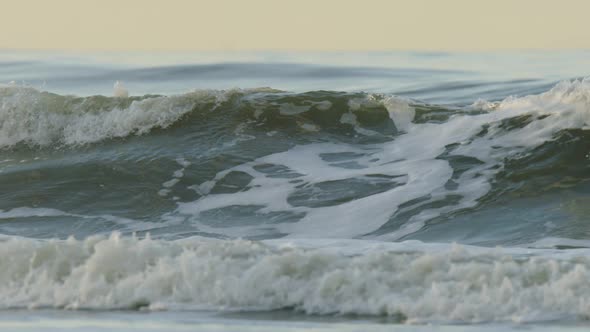Green wave roll and break in slow motion on dutch beach in sunset glow