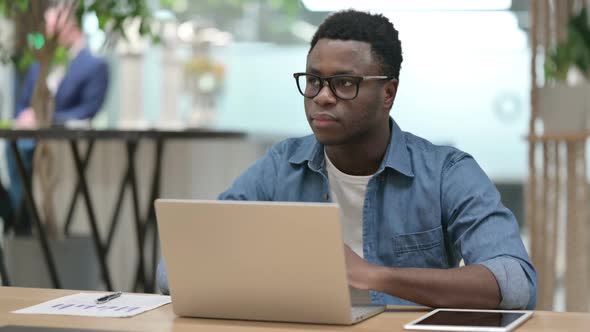 Young African Man Looking at Camera While Working on Laptop