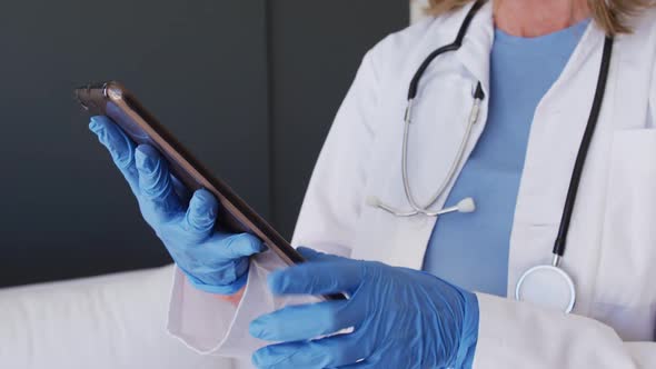 Midsection of caucasian female doctor wearing surgical gloves using tablet computer