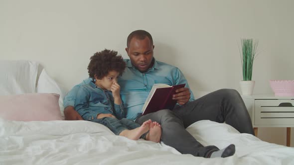 Joyful Diverse Family Reading a Book Lying on Bed