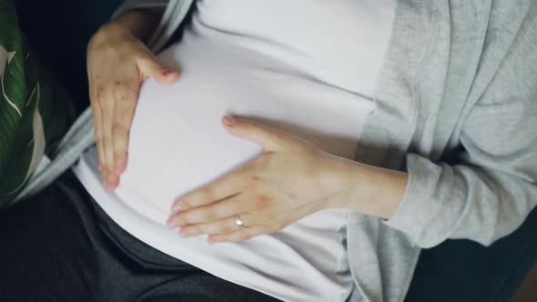 Close-up of Pregnant Belly and Tender Female Hands Caressing and Stroking Baby Bump with Tenderness