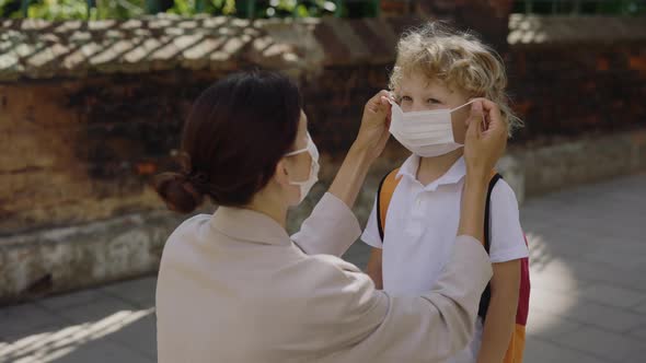 Mother Caring About Her Kid and Wearing the Surgery Mask to Her Son on the Street Before Lessons