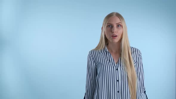 Blonde Young Woman Spreading Her Hands To the Sides and Saying "What" on Blue Background.