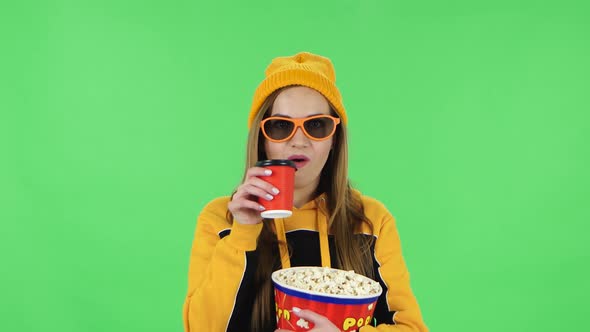 Portrait of Modern Girl in Yellow Hat in 3D Glasses Is Watching a Movie, Eating Popcorn and Drinking