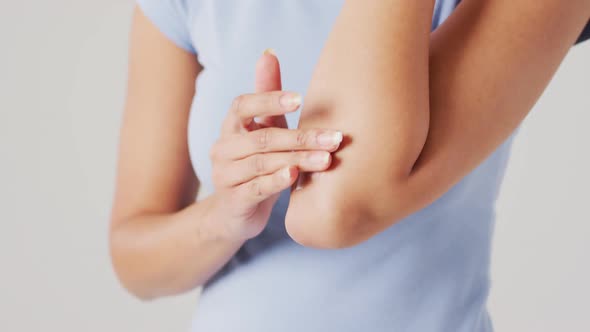 Video of biracial woman touching her arm on white background