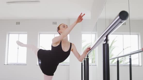 Caucasian female ballet dancer stretching up by the mirror in a bright studio