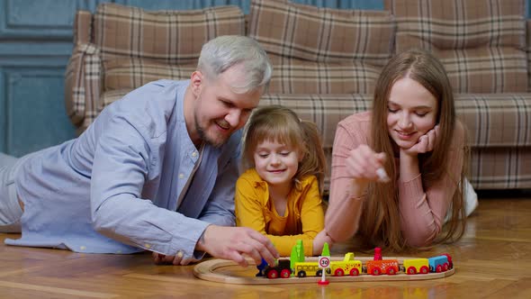 Family of Mother Father with Daughter Child Girl Riding Toy Train on Wooden Railway at Home Room