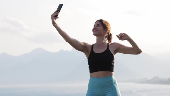 Sportive Adult Smiling Woman Standing on the Hill and Taking Selfies