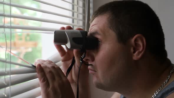 Man Spying on People Using Binoculars for Observation
