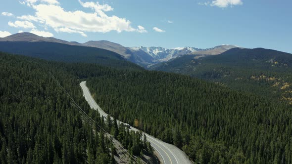 Aerial following green forest highway towards mountain range in distance, 4K