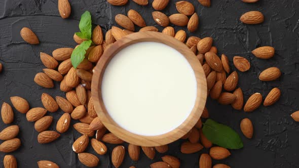 Fresh Almond Milk in Wooden Bowl and Almonds on Black Stone Background