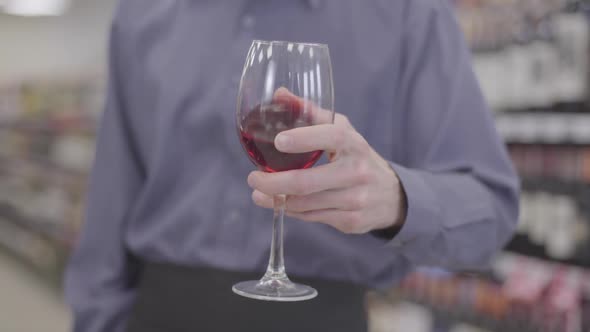 Close-up of Male Caucasian Hand Shaking Wineglass with Red Wine Inside. Unrecognizable Sommelier