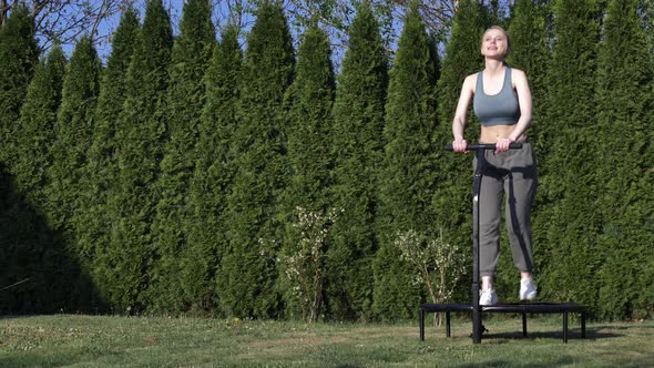 girl does Jumping fitness on trampoline in outdoor on green grass and trees on background