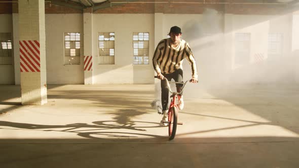 BMX rider in an empty warehouse using smoke grenade