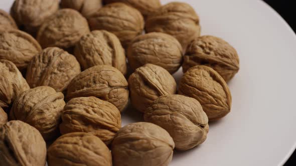 Cinematic, rotating shot of walnuts in their shells on a white surface 