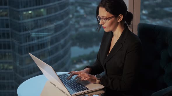 Modern Business Woman Working on a Laptop in the Evening. Portrait of Business Woman with Glasses
