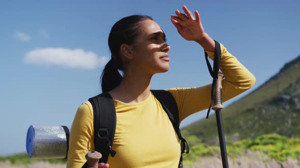 African american woman with trekking poles walking while trekking in the mountains