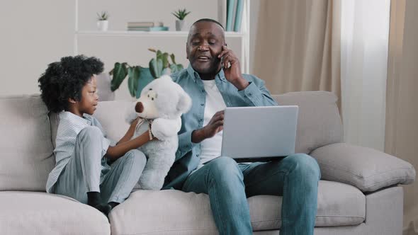 Mature African American Man Sitting on Couch Working Remotely on Laptop Answering Business Call