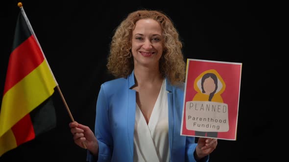 Smiling Confident Woman Holding German Flag and Planned Parenthood Funding Banner Looking at Camera