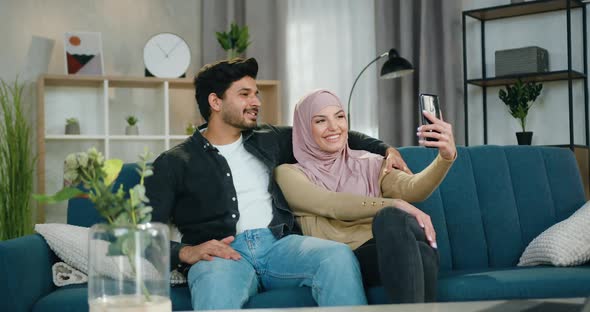 ArabicCouple Having Fun Together Sitting on Comfortable Sofa while Making joint selfie