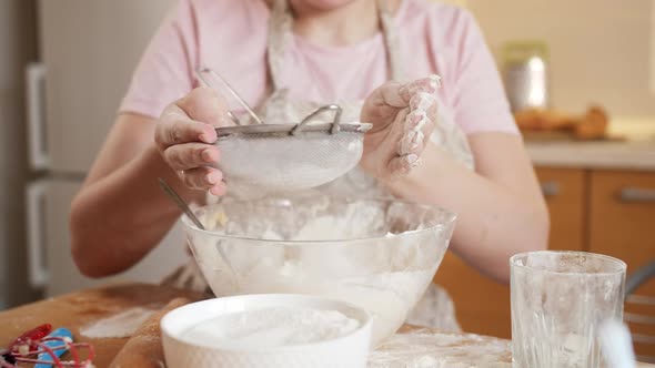 Young Woman in Apron Sifting Flour with Sieve on Kitchen at Home