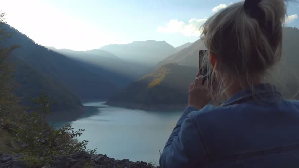 beautiful blonde takes photos or videos of a landscape in the autumn mountains.