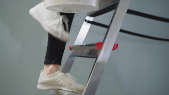 Lady Goes Up Step Ladder Holding Paint Bucket in Room