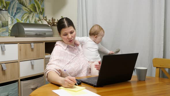 Young woman with a child talking to customer via video link and writing it down