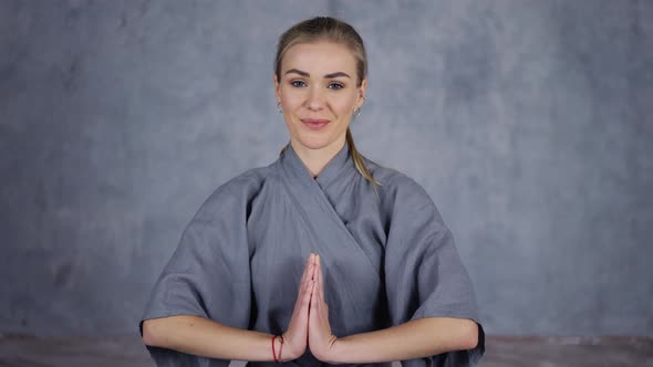 Smiling Female Coach Yoga in Robe Makes Namaste Gesture By Hands