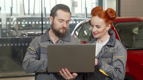 Bearded Car Mechanic Using Laptop at the Garage Working with Female Colleague