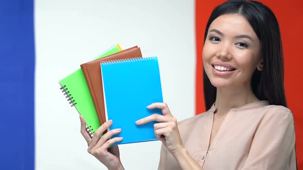 Cheerful Lady Showing Notebooks, Standing Against French Flag, Exchange Program