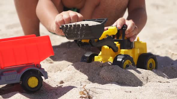 Close-up of a Child's Hands Playing in the Sand with Plastic Cars on a Sandy Beach,