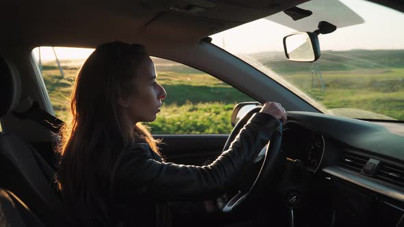 young woman driving the car outside the window beautiful sunset landscape. Slow motion
