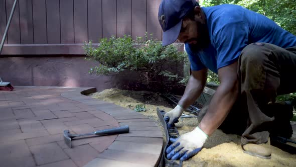 Worker takes large spike-like nails and nails the black edge retainer into place along the curving b