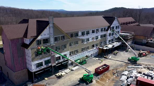 Aerial push in and descending showing Cacapon State Park lodge construction with men in cherry picke