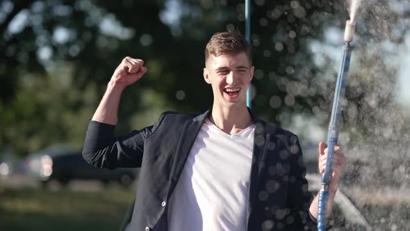 Cheerful Man Gesturing Strength Gesture Spraying Car Wash Shampoo in Slow Motion Looking at Camera