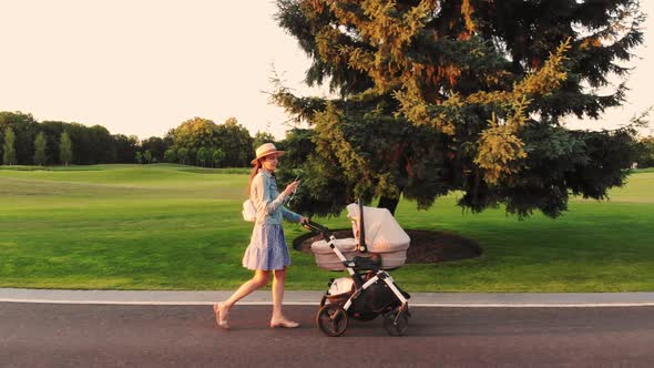 Young Modern Stylish Mother with Baby Carriage and Phone