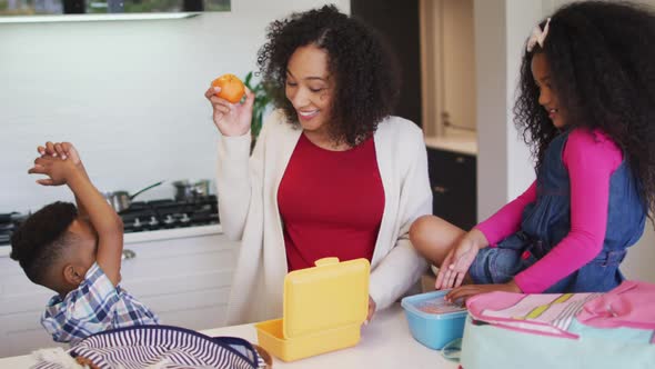 Happy african american mother packing lunch box for children to school