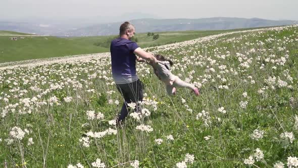 a Man is Spinning His Daughter By the Hands in a Field in Nature