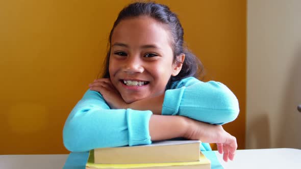 Portrait of smiling girl leaning on stack of books in classroom