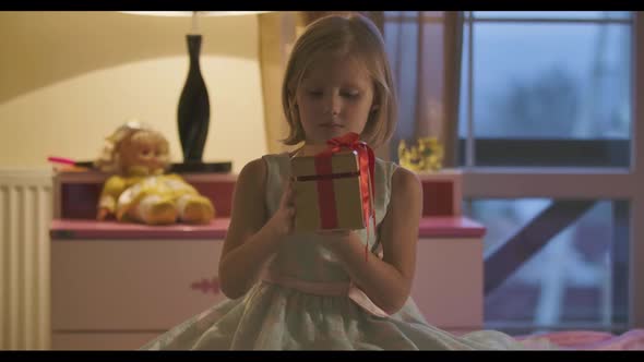 Portrait of Little Caucasian Girl Trying To Open the Casket with Red Bow