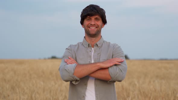 Male Farmer Crosses His Arms and Looks at the Camera Against the Background of a Wheat Field