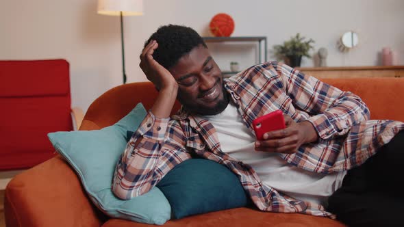 Cheerful Young Man Lying on Sofa Using Mobile Phone Share Messages on Social Media Application