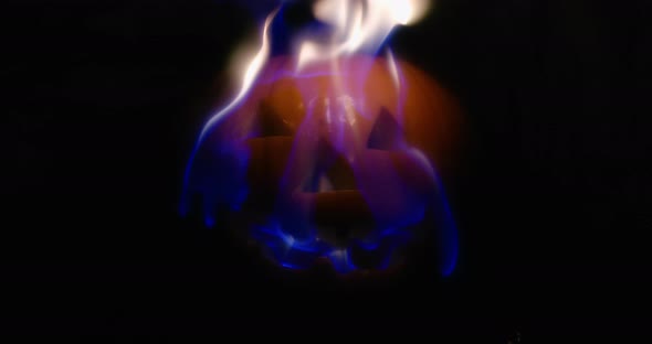 Slow motion medium shot of a jack-o-lantern as its face burns.