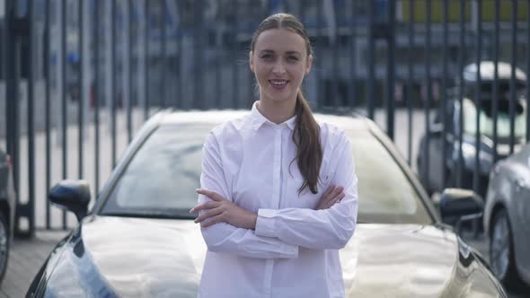 Portrait of Satisfied Wealthy Rich Woman Crossing Hands Looking at Camera Standing at Black New Car